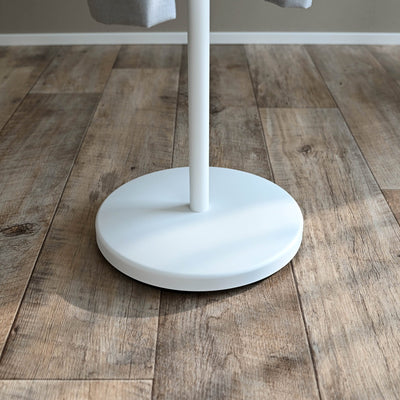 Close-up of the white Yamazaki Home Coat Rack (70" H) - Steel circular base resting on wood-plank flooring, with the slender pole rising from its centre.