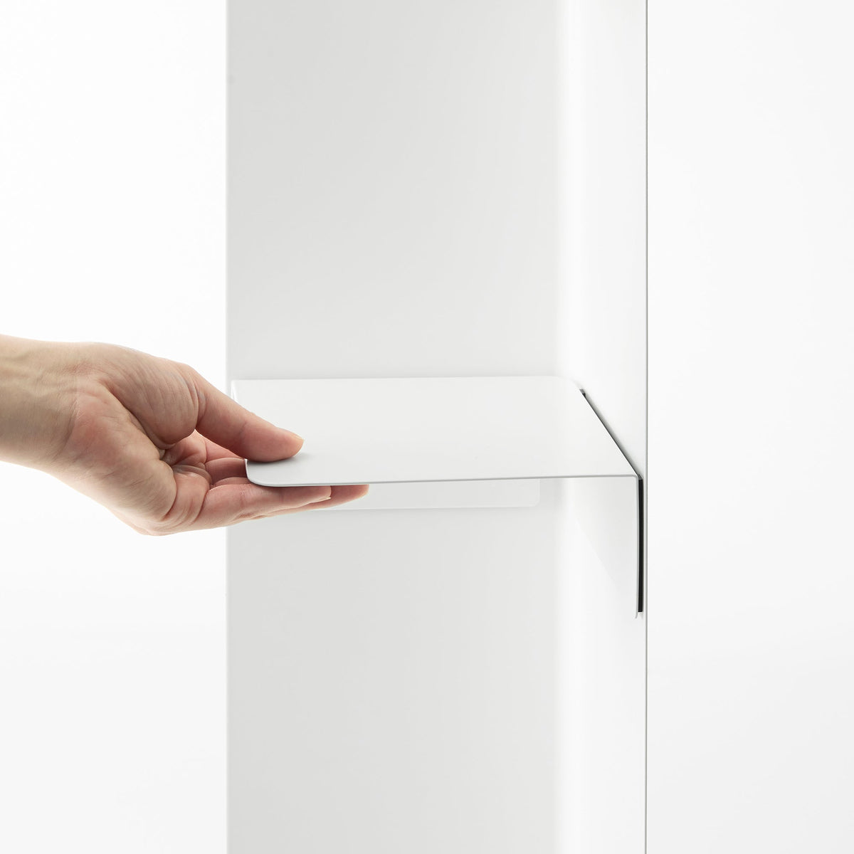 A hand slides the white shelf component of the Yamazaki Home Rolling Bathroom Organizer - Steel into position against the upright panel, showing its folded edges.